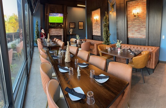 Tables and seating inside the Clubhouse private event space in Edwardsville, with a TV on the wall and windows along one side
